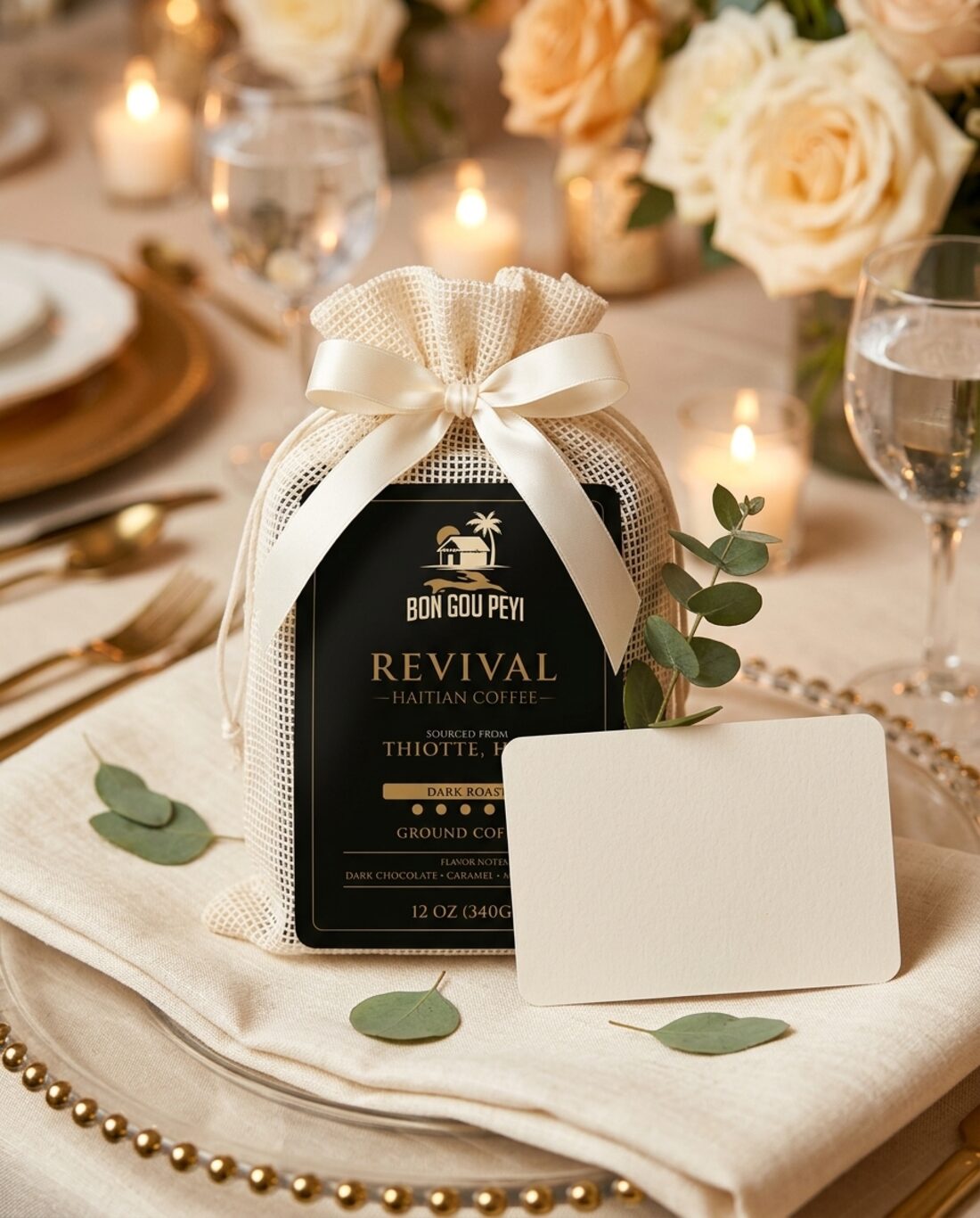 A Revival coffee bag in an ivory mesh favor pouch tied with ribbon, with a blank card and eucalyptus at a candlelit place setting